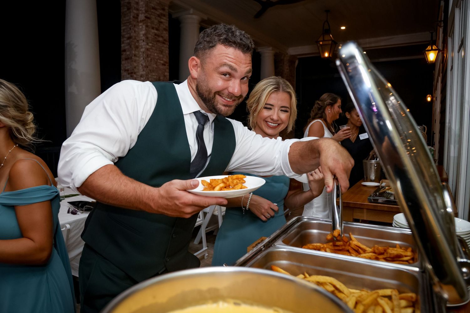 Wedding guests serve themselves from a buffet line at an indoor reception venue.