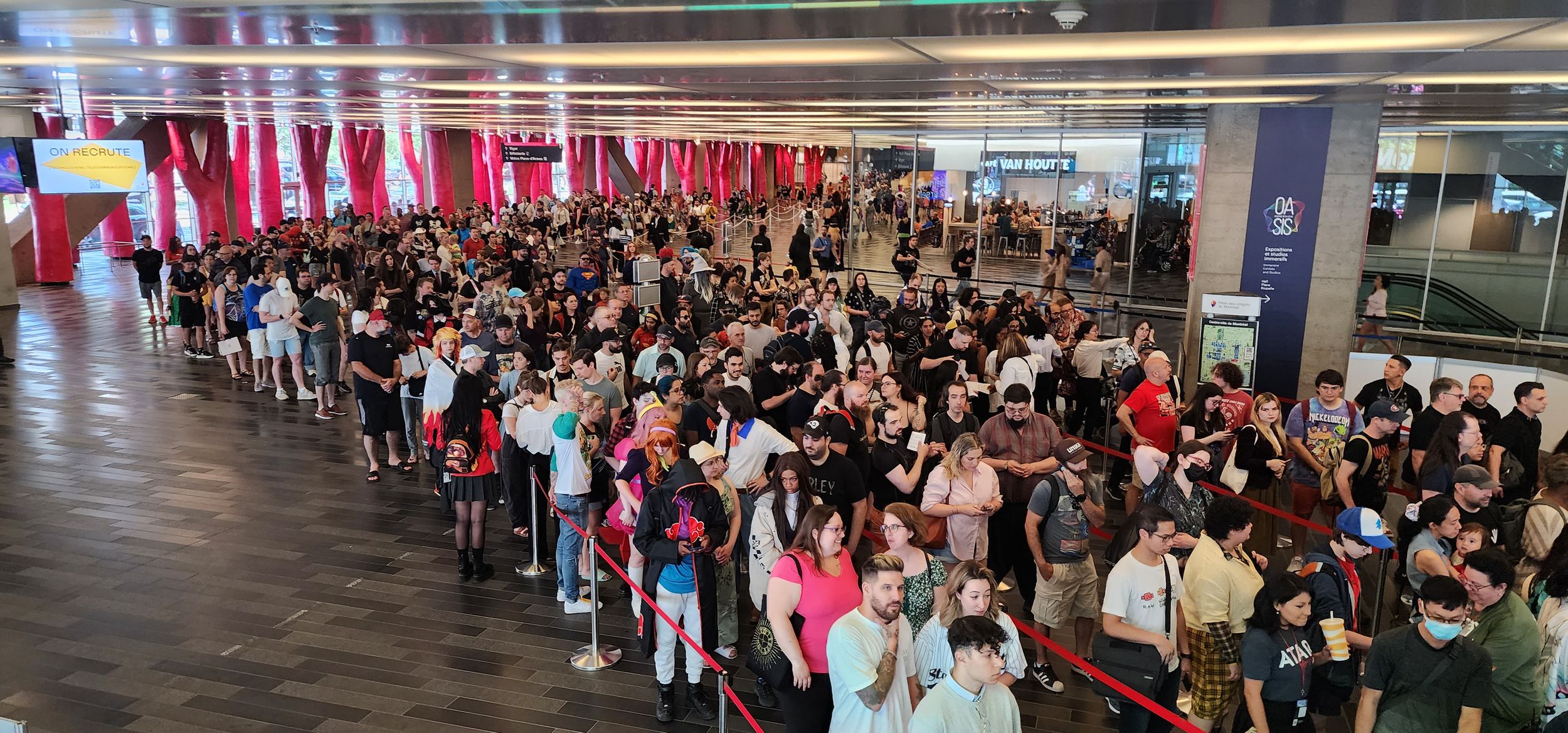 Large crowd of people waiting in line at an indoor event space with red banners.