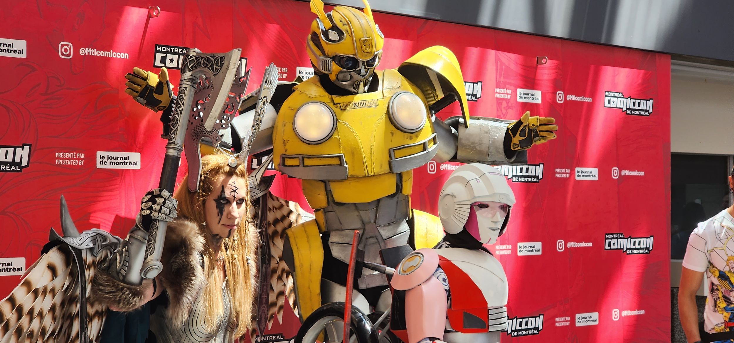 Cosplayers posing against a red backdrop at a convention.