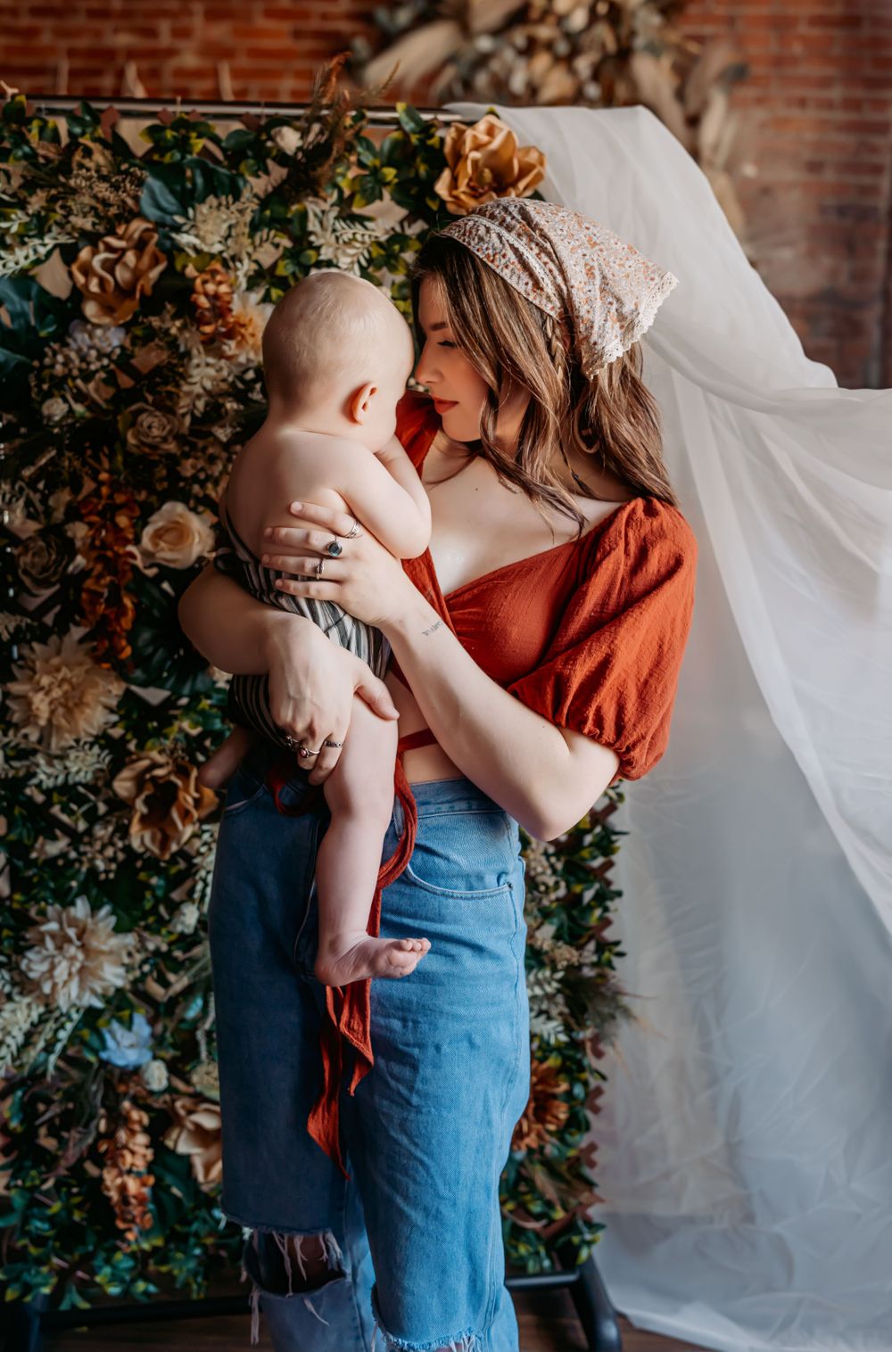 A tender maternal moment against floral backdrop with baby wearing striped outfit.