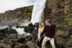 A couple shares an intimate moment by a majestic waterfall cascading down rocky cliffs in nature.
