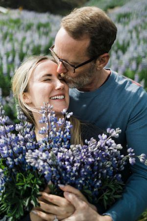 A couple shares an intimate moment while holding purple lupine flowers.