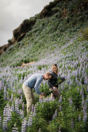 A couple shares a playful moment among blooming purple lupine flowers on a hillside.