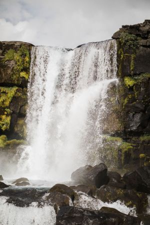 Powerful waterfall cascades down moss-covered rocky cliffs with white rushing water.