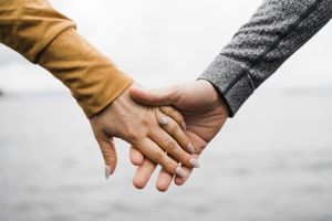 Close up of two hands holding each other against a blurred background.