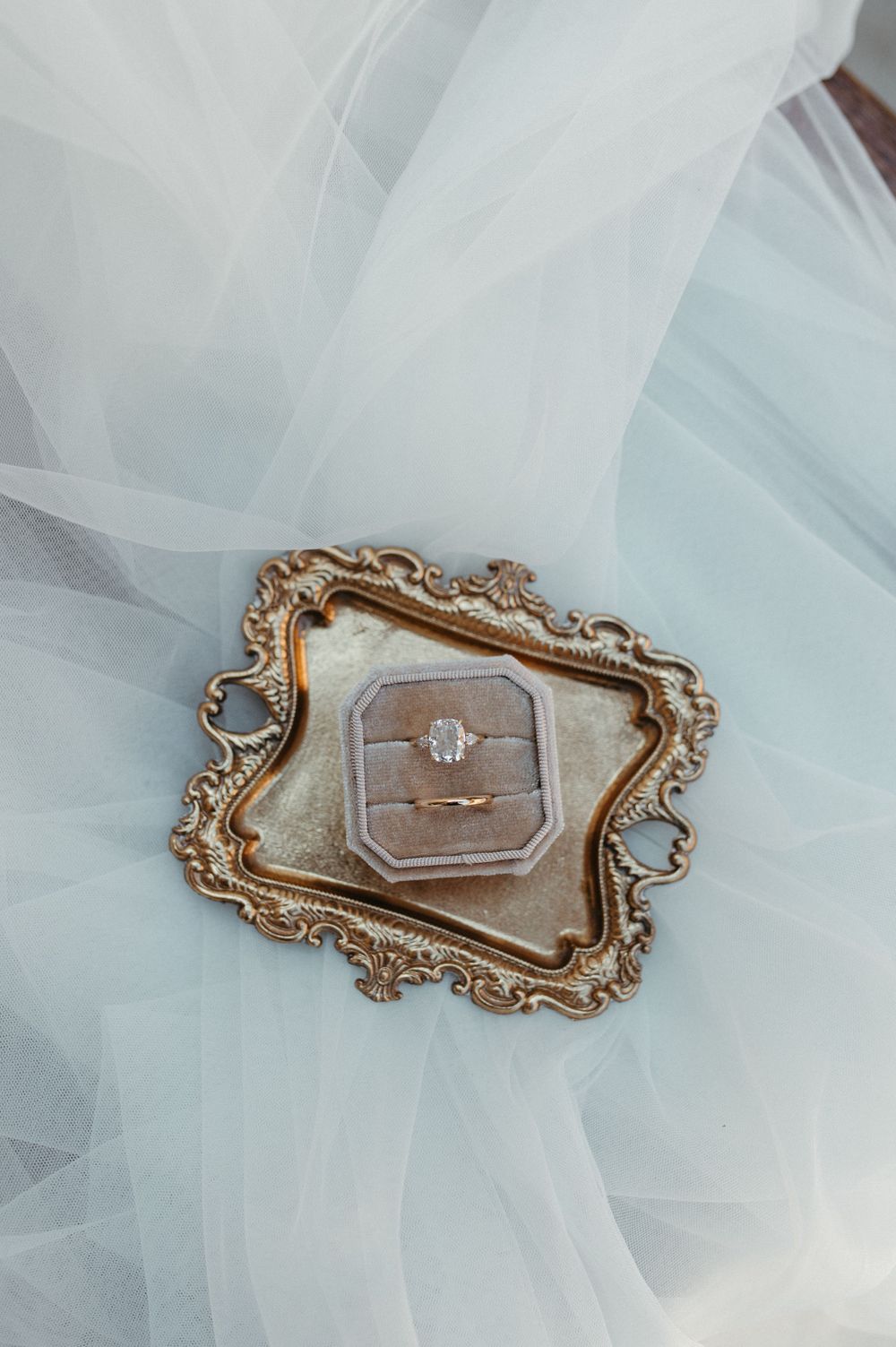 Engagement ring in ornate gold vintage ring box on white tulle fabric.