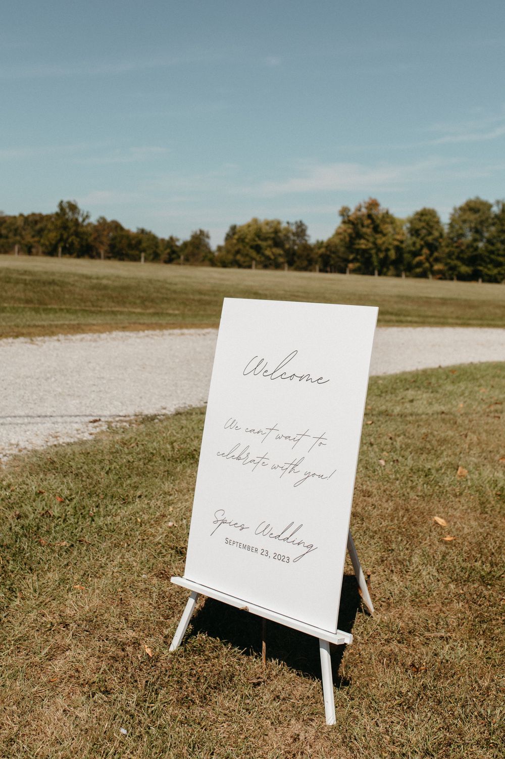 Welcome sign on white easel stand displayed on grassy outdoor venue.