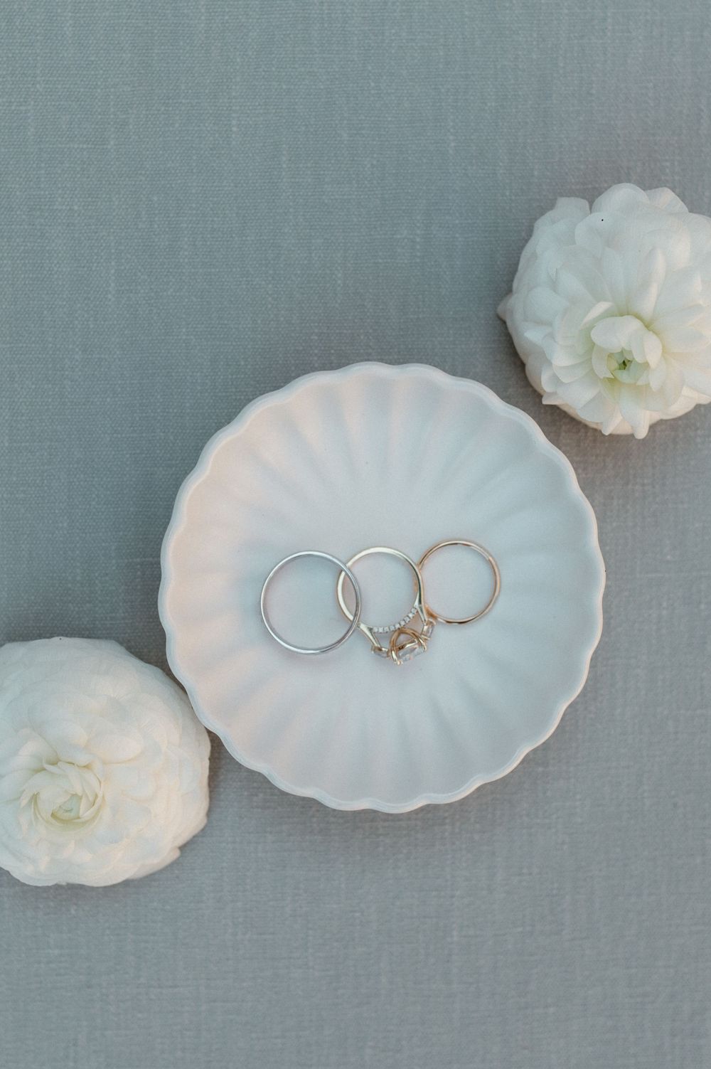 Wedding rings displayed on a white scalloped dish with delicate white flowers.