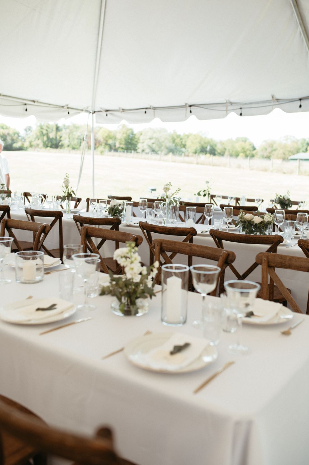 Elegant wedding reception tables set under a white tent with wooden crossback chairs and lakeside view.