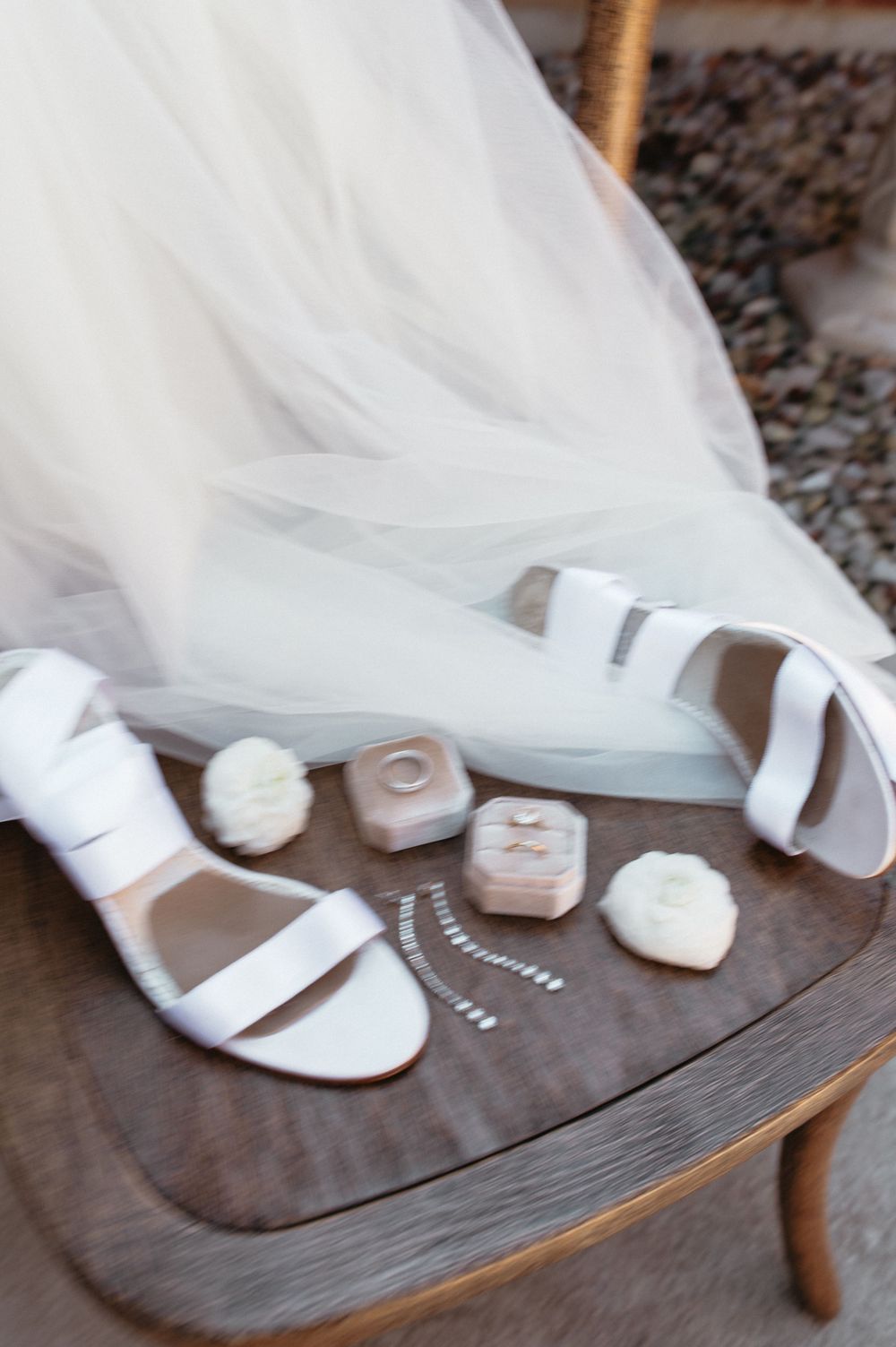 Bridal details featuring white strappy sandals and wedding accessories on wooden furniture.