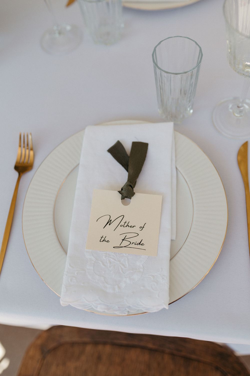 Place setting with white plate, gold flatware and name card tied with dark ribbon.