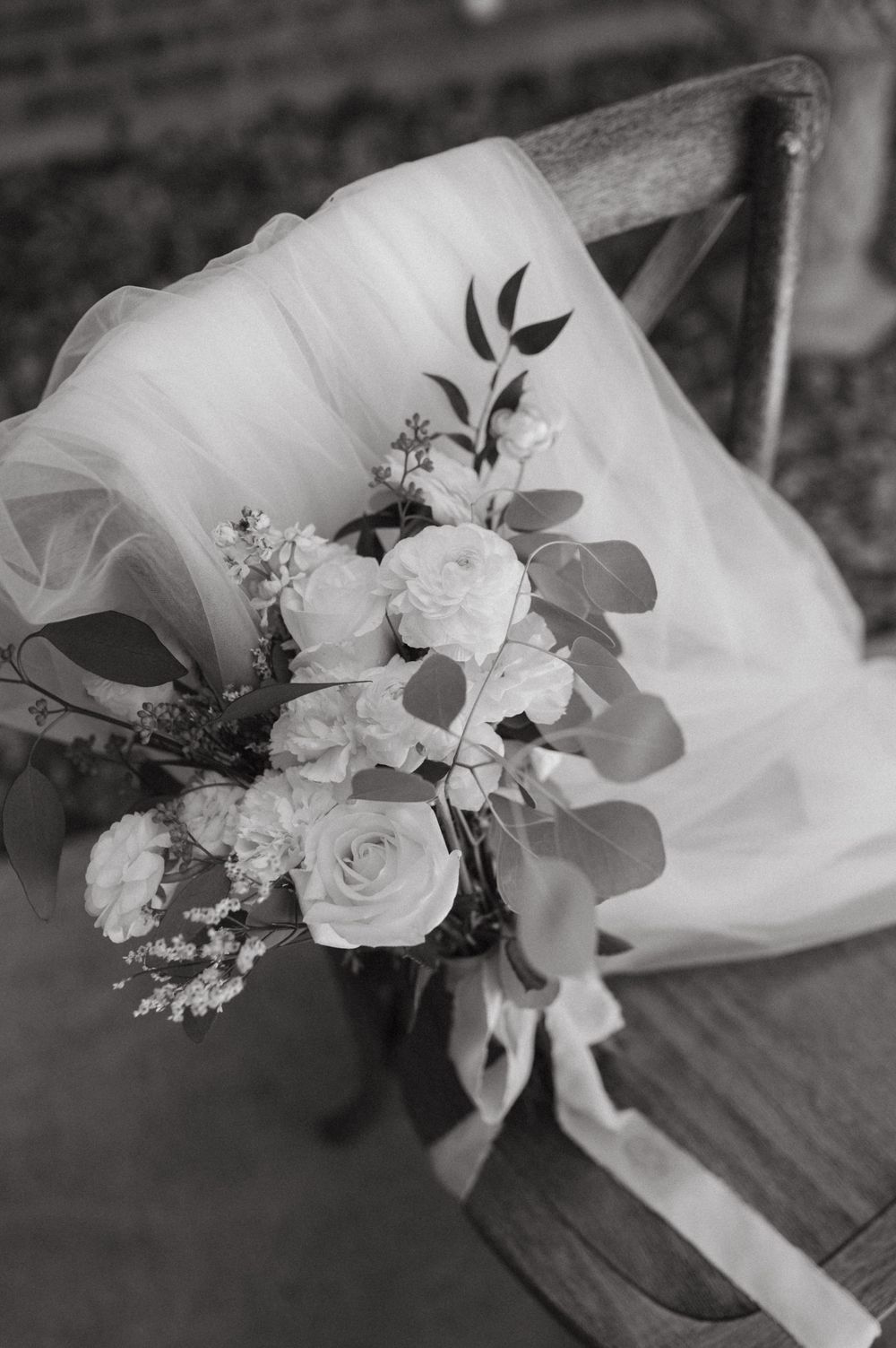 Black and white image of romantic wedding bouquet with roses and eucalyptus on wooden chair.