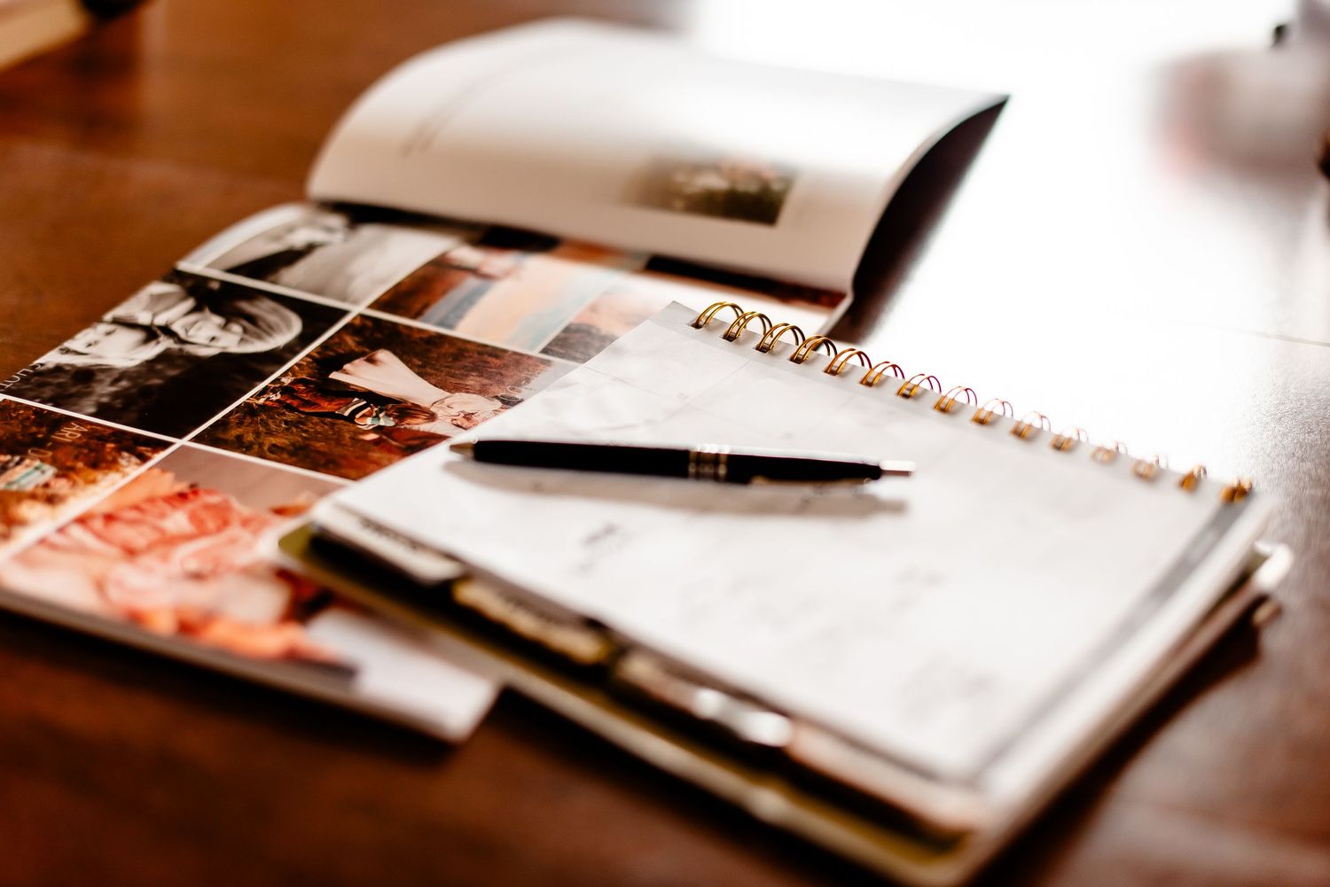 Wedding planning notebook with photos and pen on wooden table.