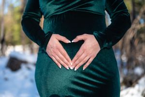 Hands forming a heart shape over a pregnant belly in an elegant emerald velvet dress.