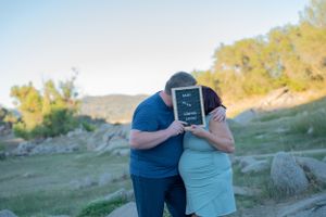 Couple holding black letterboard sign together outdoors among rocky landscape.