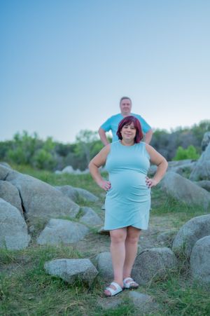 Couple poses together among large boulders in outdoor setting at sunset.
