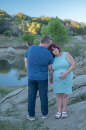 Couple embracing near water's edge with rocky landscape in background.