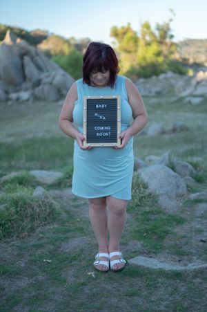 Person in light blue dress holds letterboard announcement sign near rocky terrain.