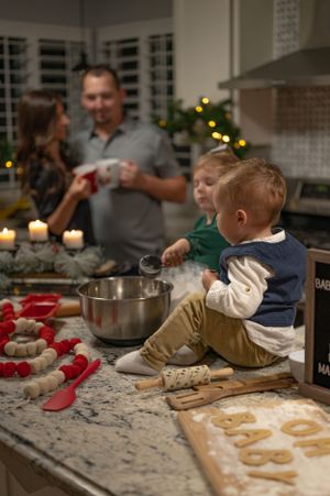 A toddler helps with baking while sitting on a counter with cookie ingredients and decorations.