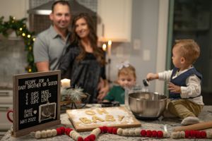 A family bakes cookies together in their kitchen with holiday decorations visible in the background.