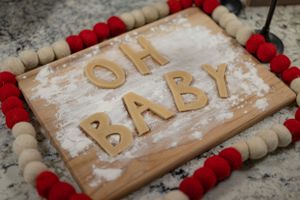 'OH BABY' spelled out in flour on a wooden board surrounded by red and natural wooden beads.