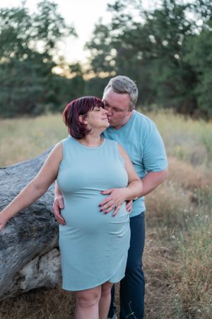 An intimate maternity photo shows a couple sharing a tender moment against a rustic outdoor backdrop.
