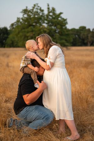A heartwarming family moment captured in a sunlit field during a maternity photoshoot.