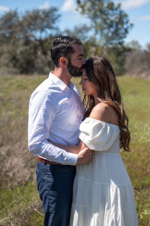 A romantic couple shares an intimate moment in a spring meadow wearing coordinated white and blue outfits.