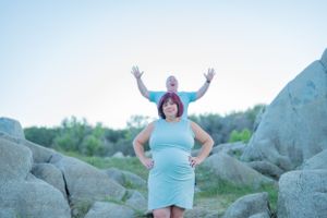 Fun pregnancy announcement photo with couple posing playfully by rock formation.