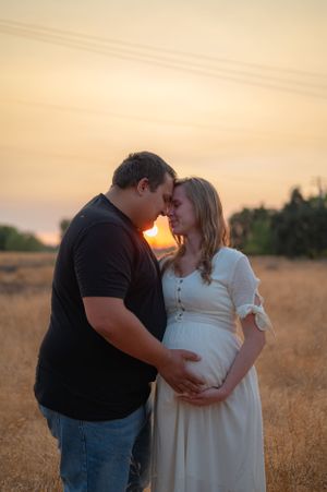 A romantic sunset maternity photo of a couple sharing an intimate moment in a field.