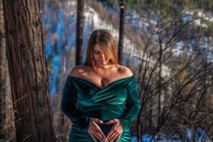 An intimate maternity moment captured in a forest setting with a luxurious emerald dress.