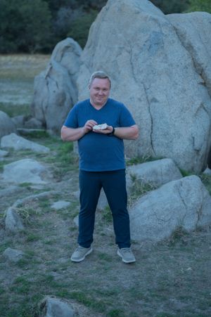 Person in blue shirt stands against large boulder formation at dusk.
