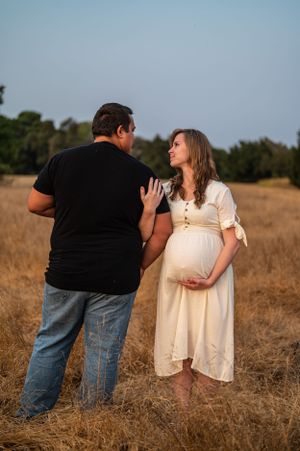 A romantic maternity photo of a couple sharing a moment in a dry grass field at golden hour.