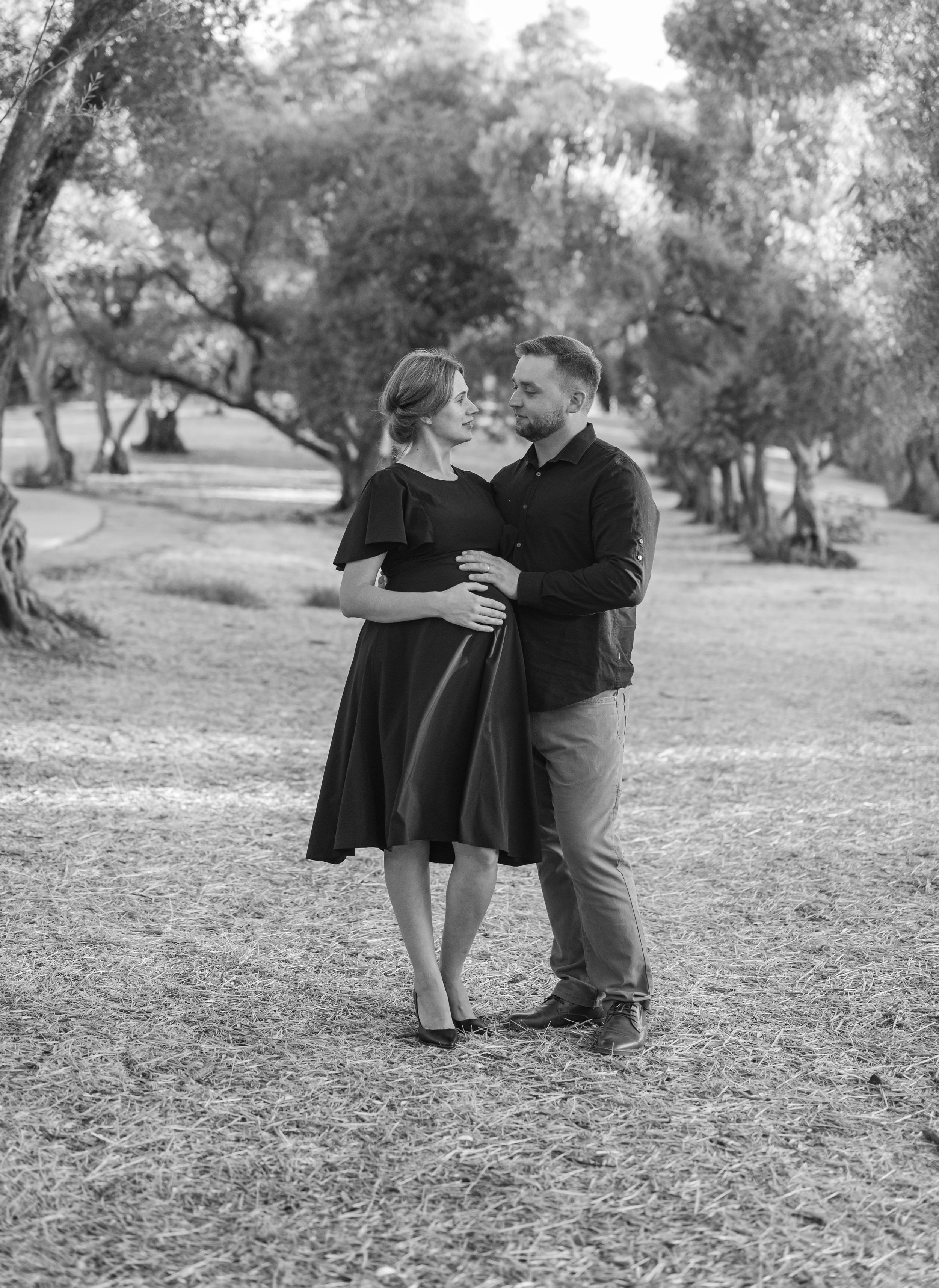 A couple shares a tender moment while standing in a sunlit grove.