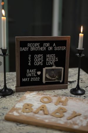 A pregnancy announcement sign with recipe and ultrasound photo flanked by candlesticks.