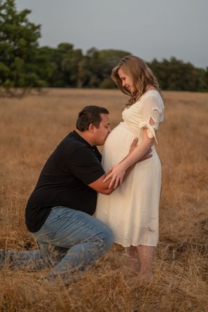 A tender maternity photoshoot in a golden field at sunset captures an intimate moment between a couple.