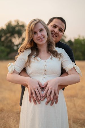A maternity portrait of a couple embracing in a golden field at sunset.