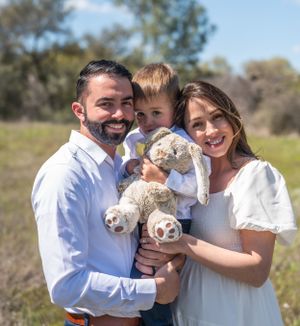 Happy family poses outdoors with their child holding a stuffed animal.