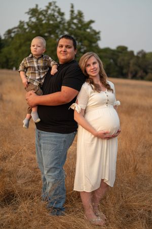 Family standing together in a sun-lit field during a maternity photo session.
