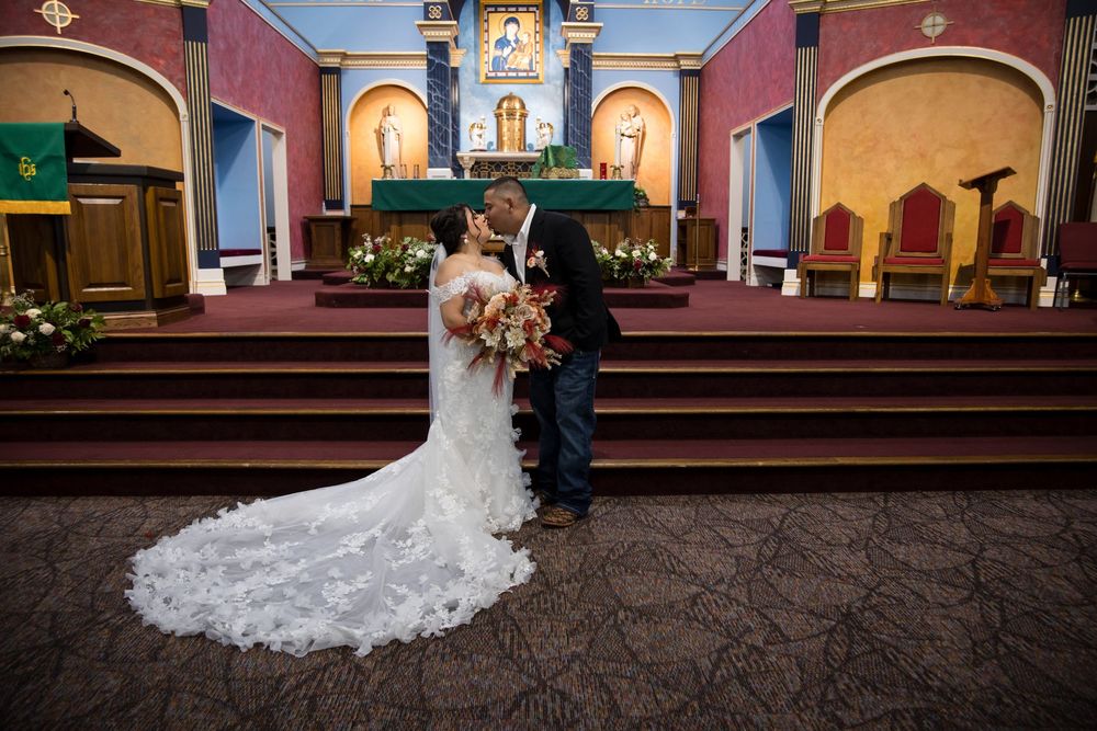 Newlyweds sharing their first kiss at the altar of a traditional Catholic church during a wedding ceremony. Wide-angle shot showcasing the b