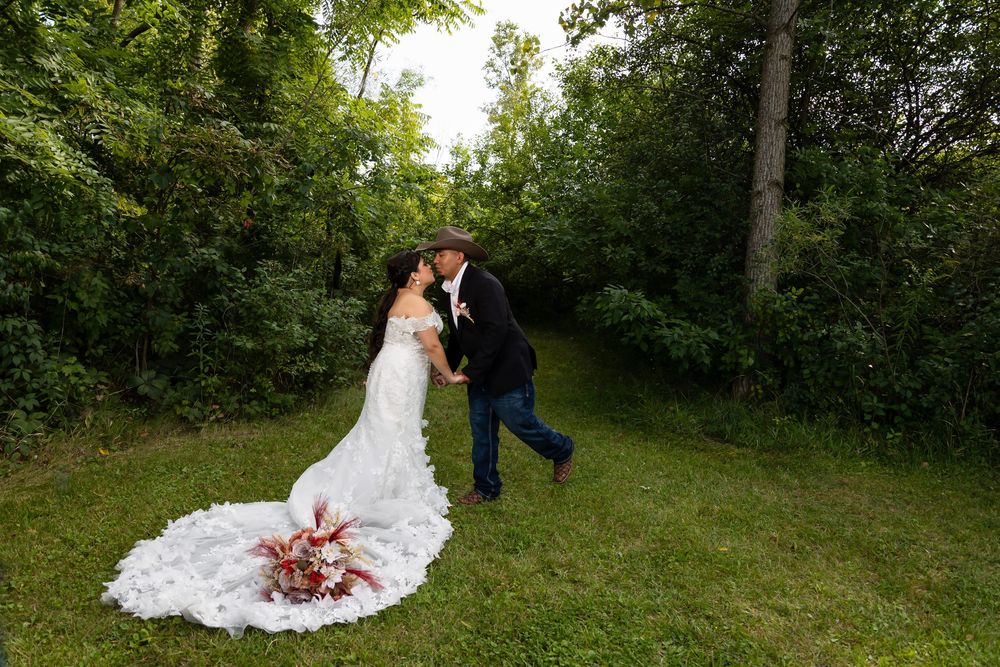 Candid moment of a groom kissing his bride on the forehead in a scenic outdoor park setting. The photo captures the full detail of her long
