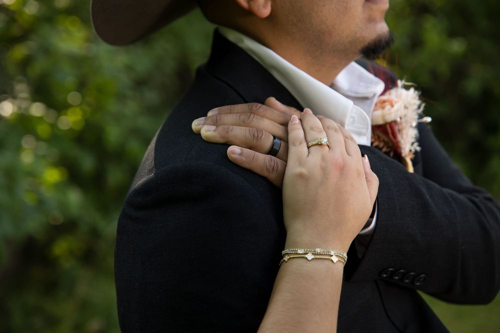 Close-up of a bride's hand with a gold bracelet and wedding ring resting on the groom's shoulder during a Lake County wedding. Professional