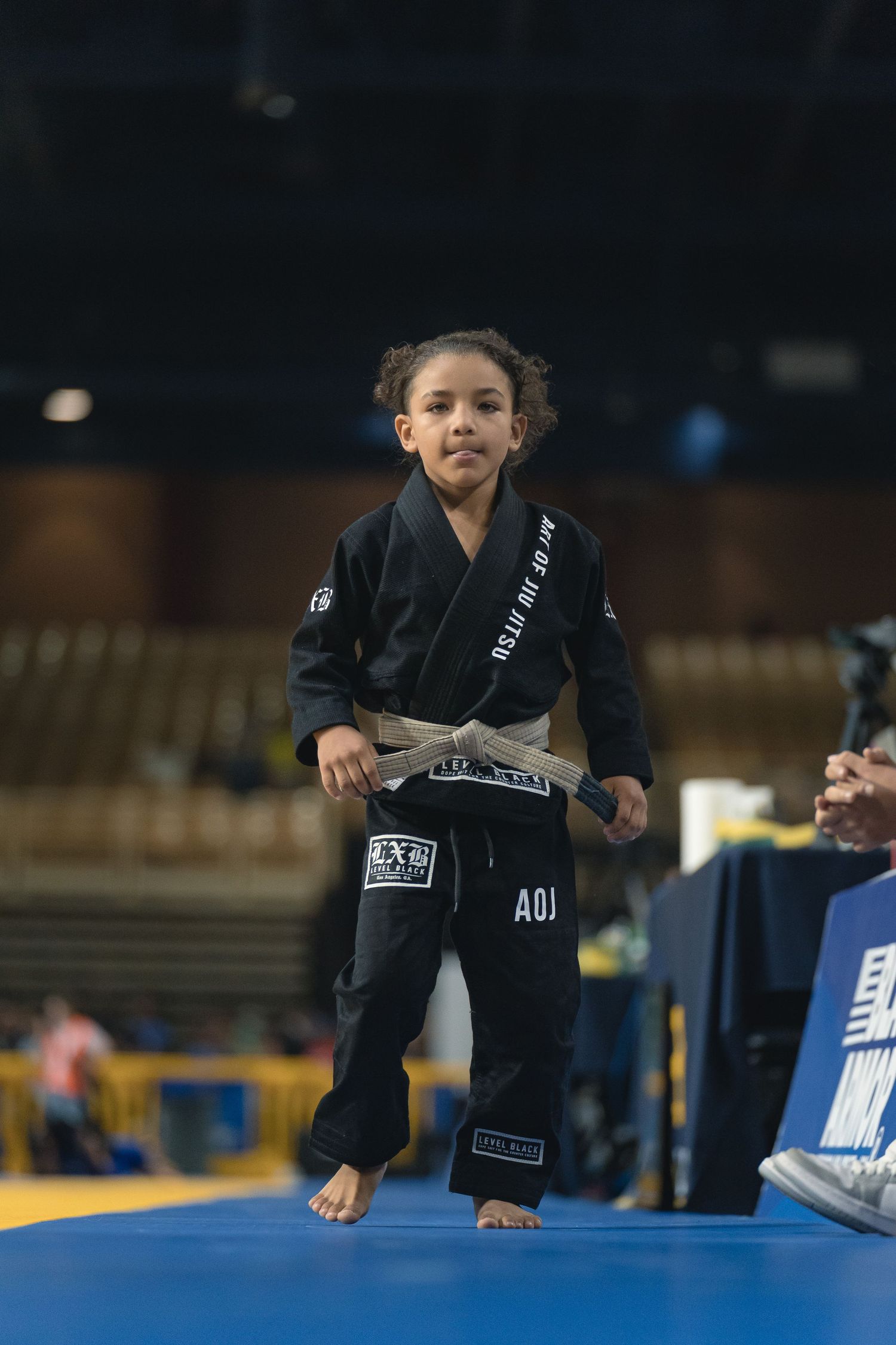 Young martial arts competitor stands on blue mat wearing black gi uniform.