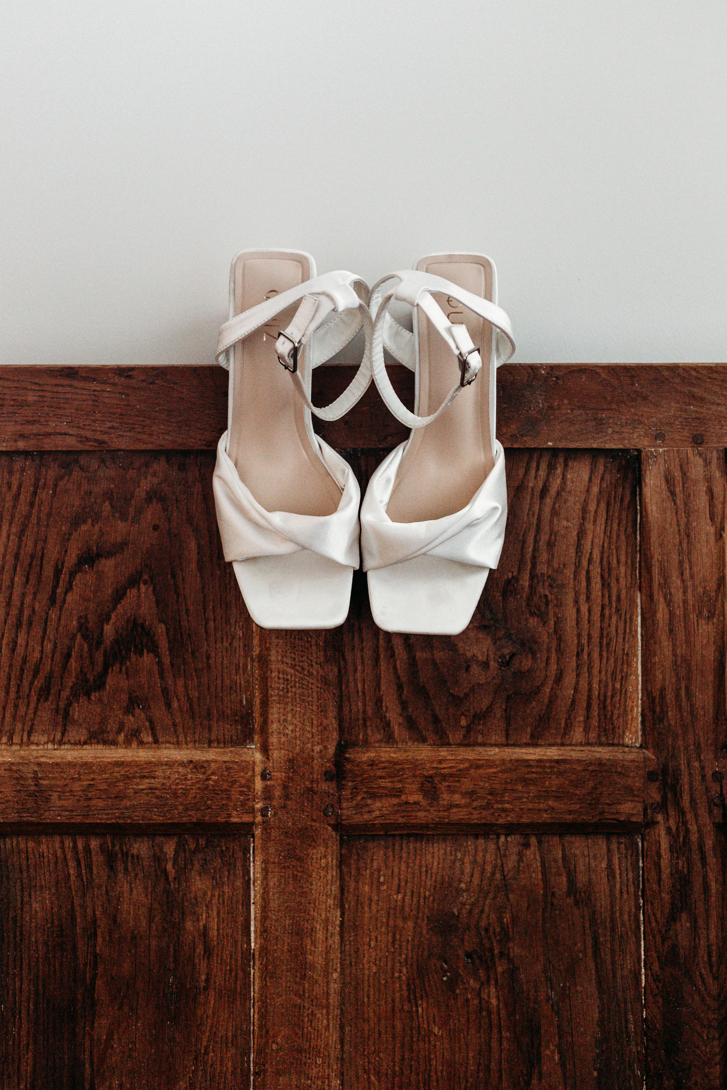 Elegant white bridal sandals with ankle straps resting on a dark wooden surface.