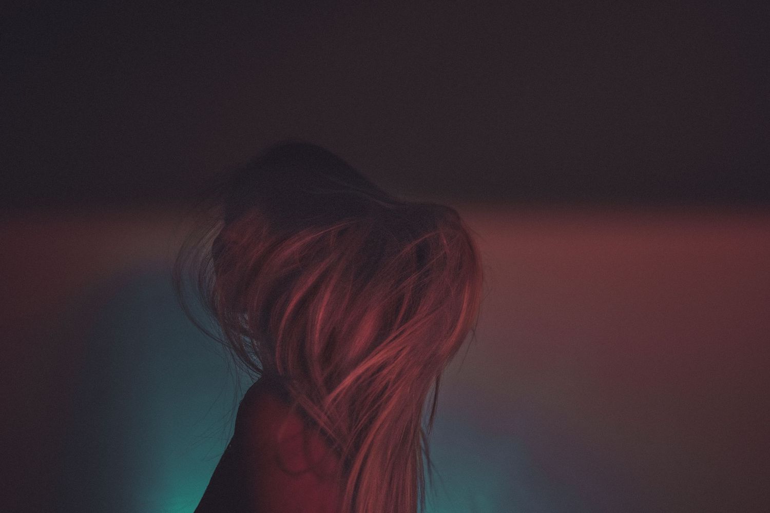Silhouette of flowing hair against a dark background with red and teal lighting.