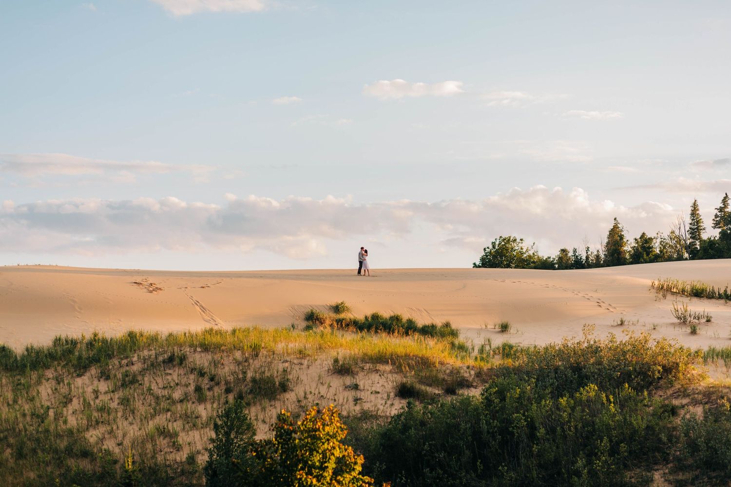 A couple embraces on top of Sleeping Bear Sand Dunes at Sunset by Traverse City Photographer Grace Hudson