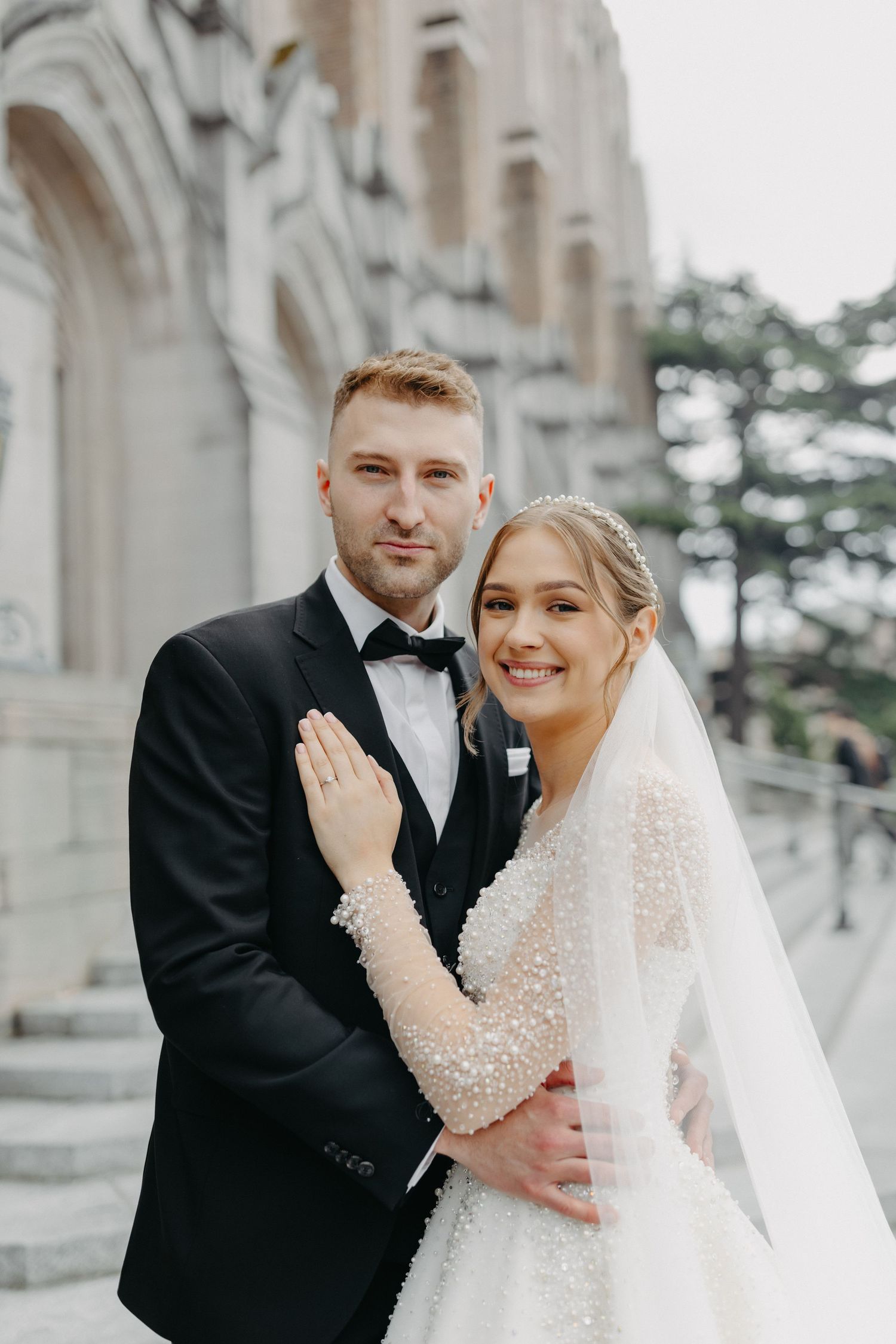 Happy wedding couple poses against Gothic stone architecture in natural light.