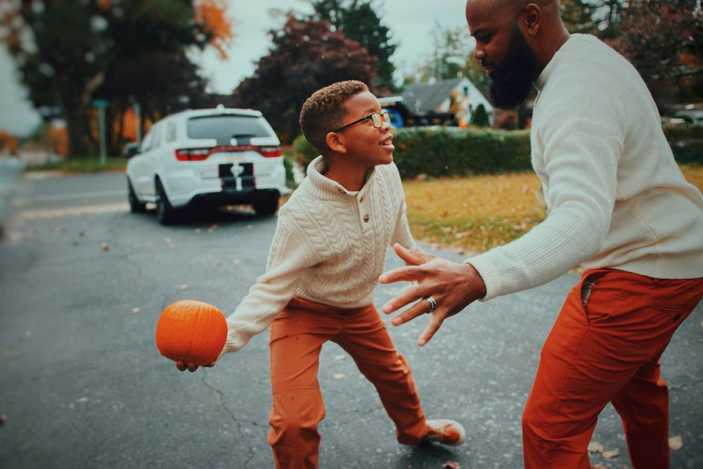 People playing and chasing with an orange pumpkin in a fall outdoor setting.