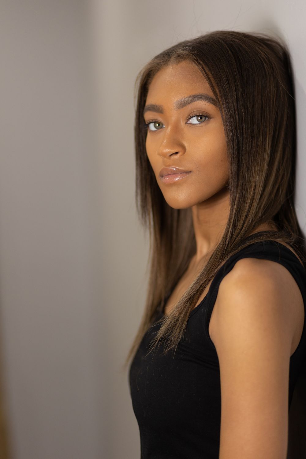 Studio beauty shots in black sleeveless top against neutral background.