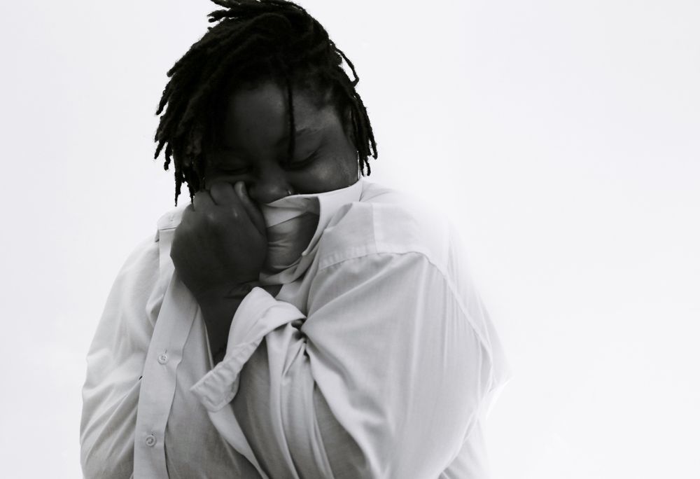 Artistic black and white portrait of a person in a white shirt with dramatic lighting and emotional pose.